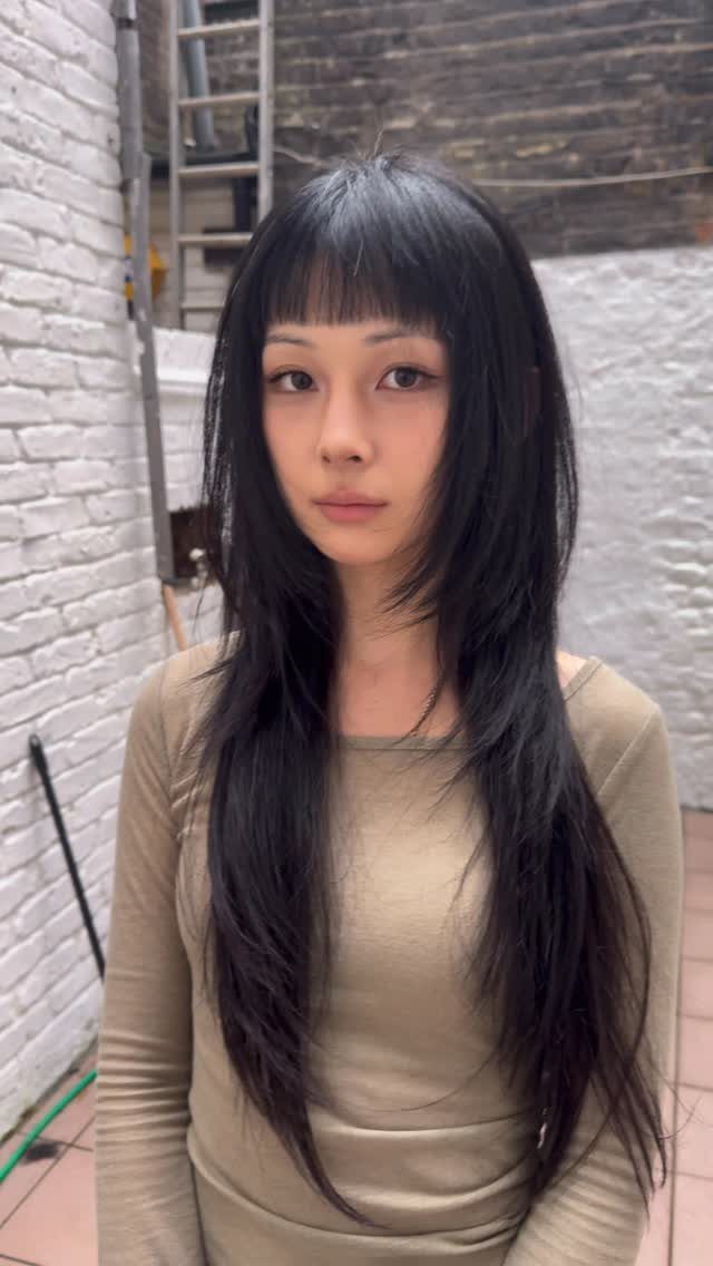 Woman showing long black hair with soft feathered bangs in a brick passage