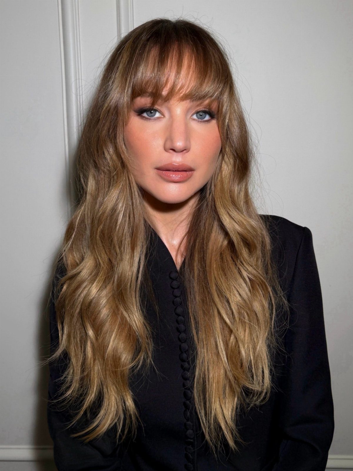 Woman with long wavy light-brown hair and a soft, full fringe