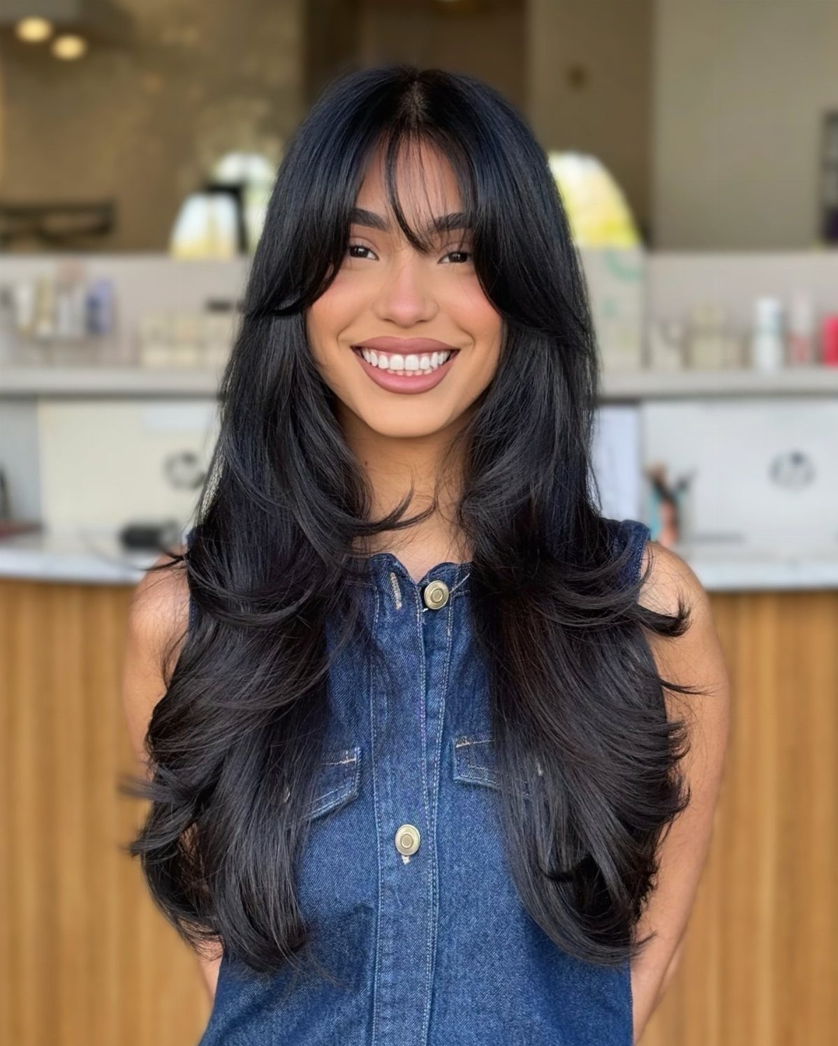 Woman showing long dark layered hair with wispy bangs in a salon