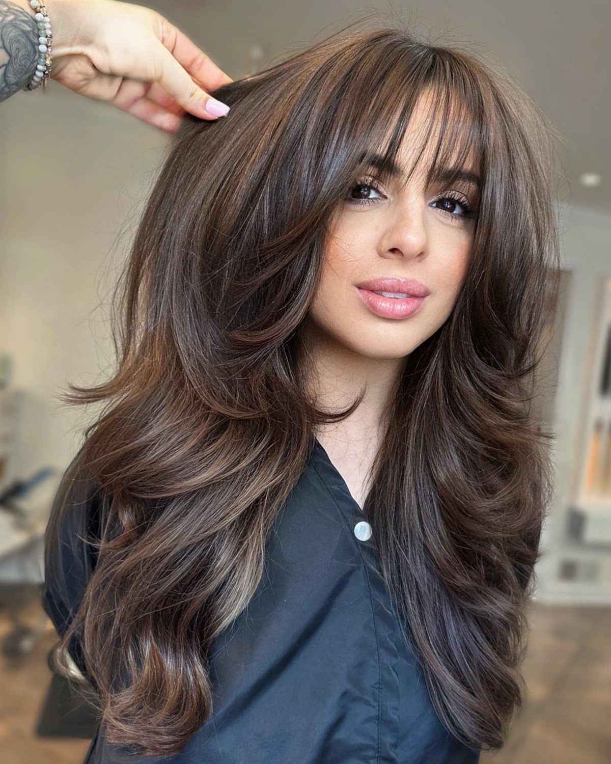 Woman displaying long brown swoopy bangs and voluminous layered hair