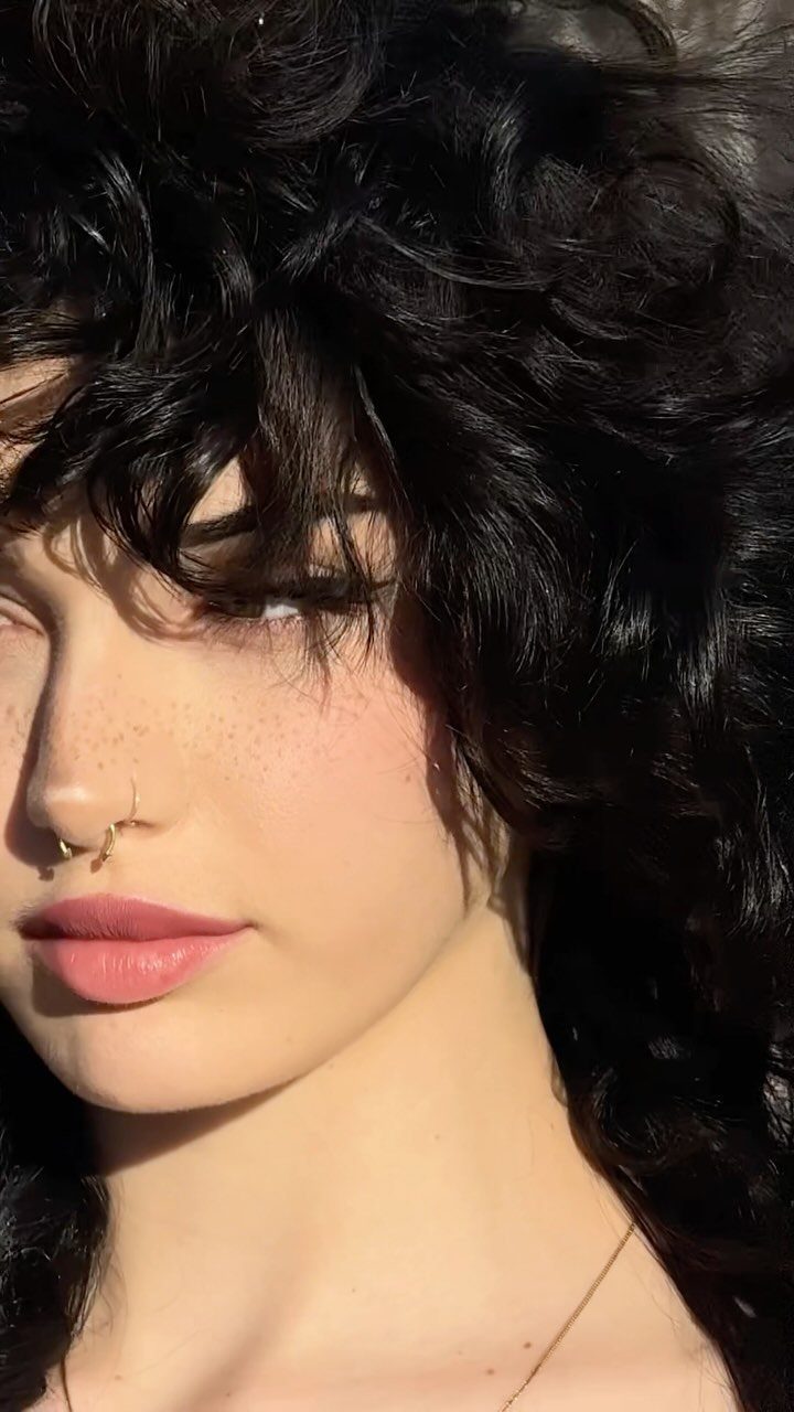 Dark curly shag haircut with tousled, piecey bangs framing the forehead