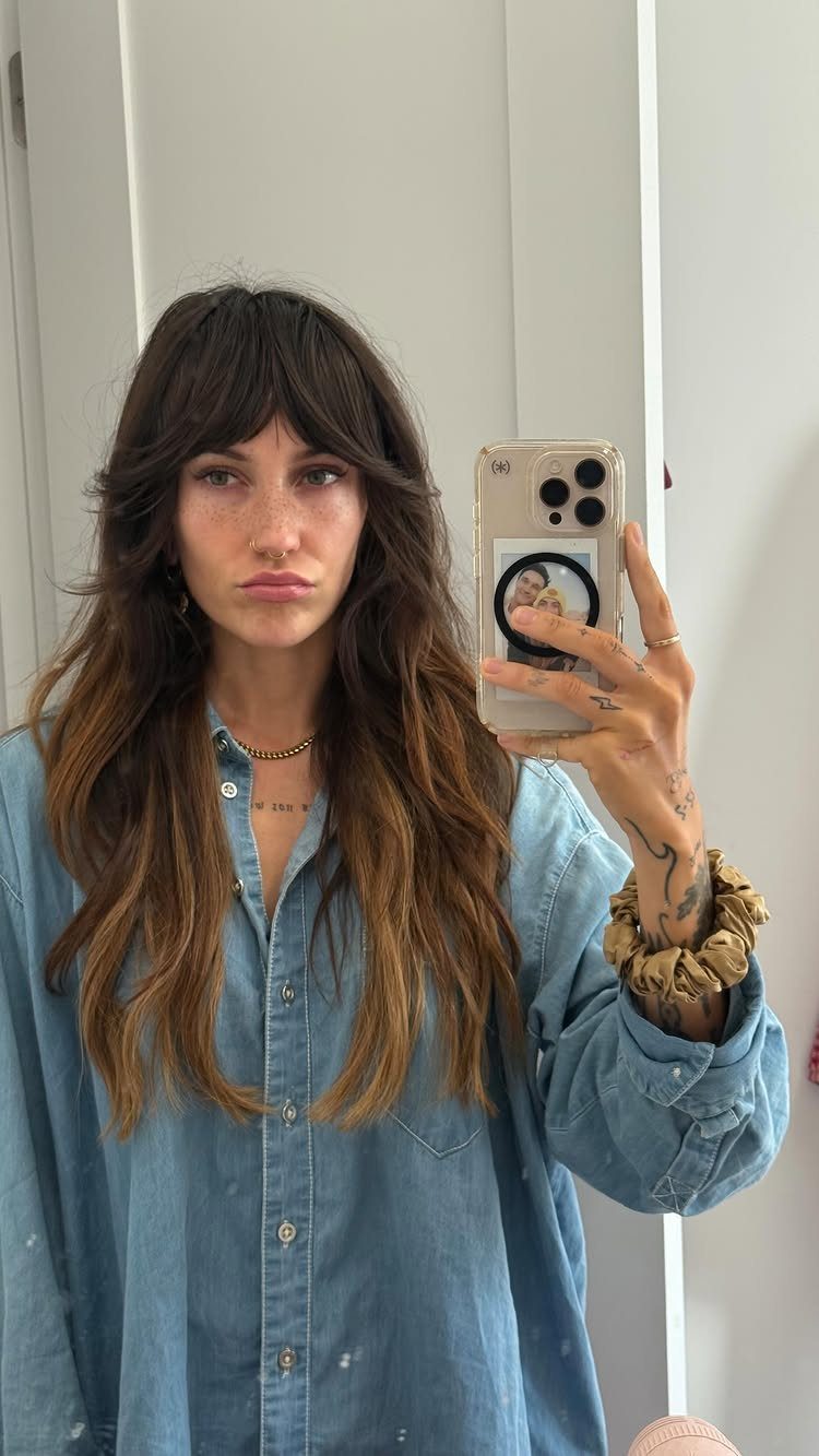 Woman with long brown hair and center-parted curtain bangs taking a mirror selfie