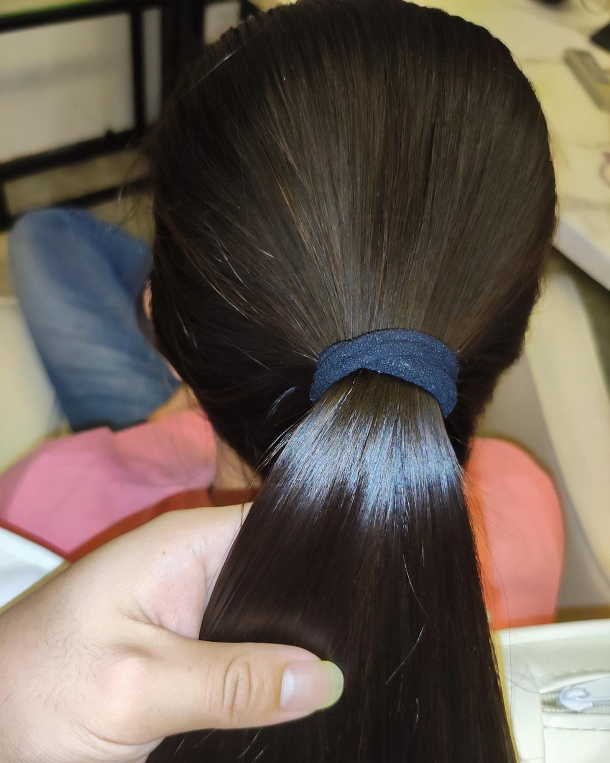Sleek dark hair pulled smoothly into a low ponytail with a blue tie