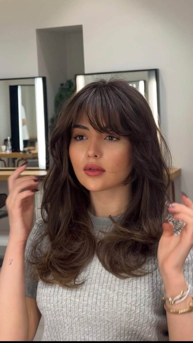 Woman with long layered brown hair and softly arched bangs in a salon