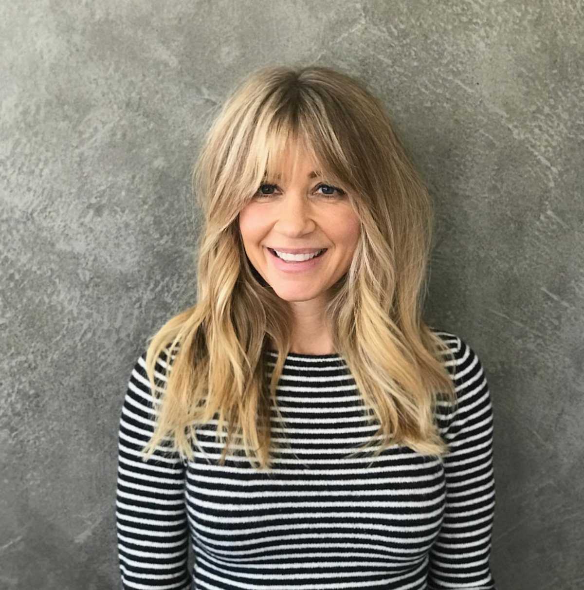 Woman with voluminous blonde hair and wispy, center-parted Bardot bangs