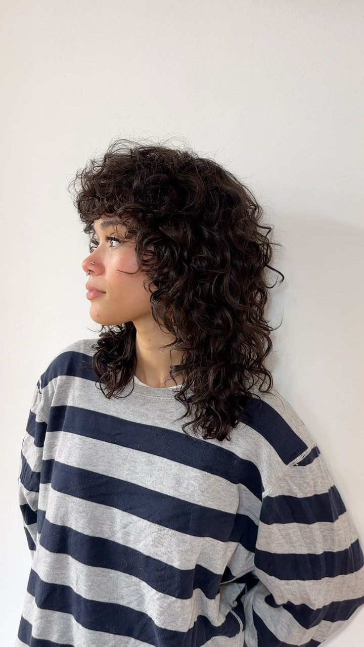 Curly shag haircut with full bangs on a person wearing a striped shirt