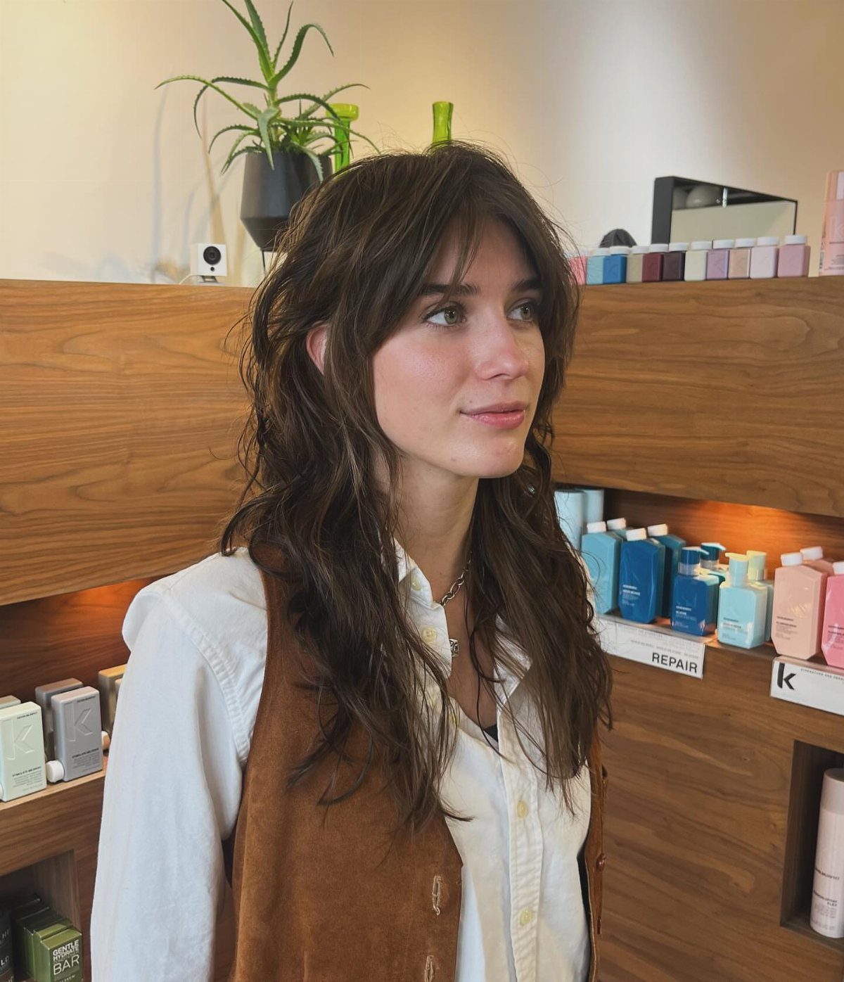 Woman with long layered dark hair and wispy curtain bangs in a shop