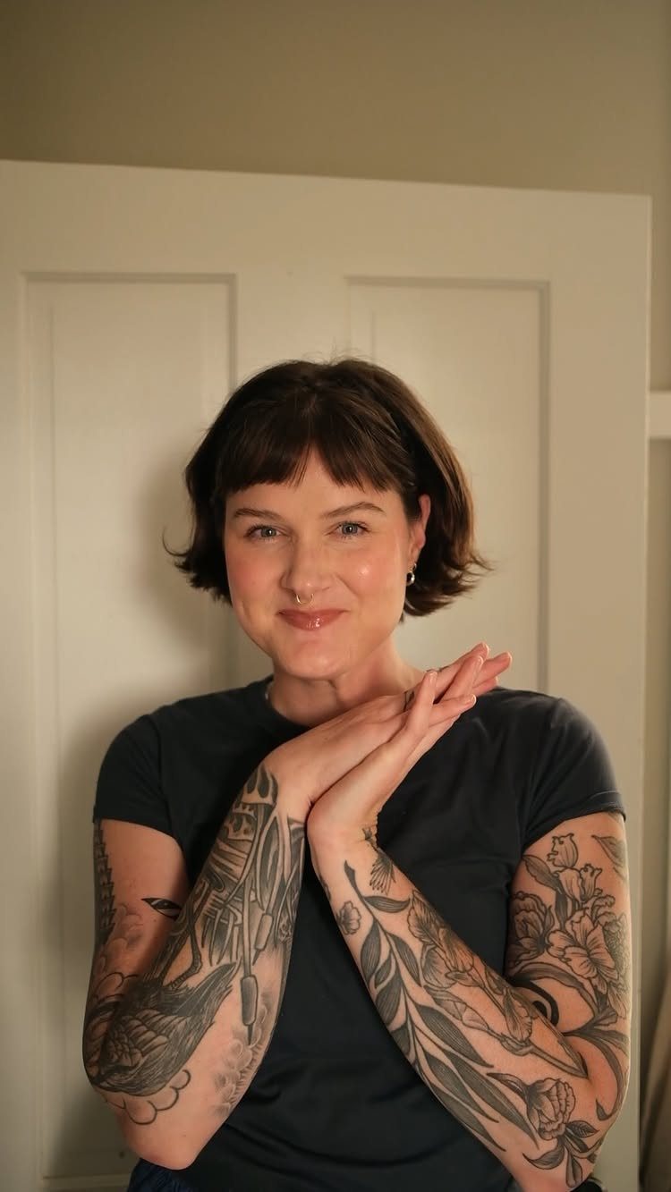 Woman with a short dark bob and curved bangs posing before a paneled door