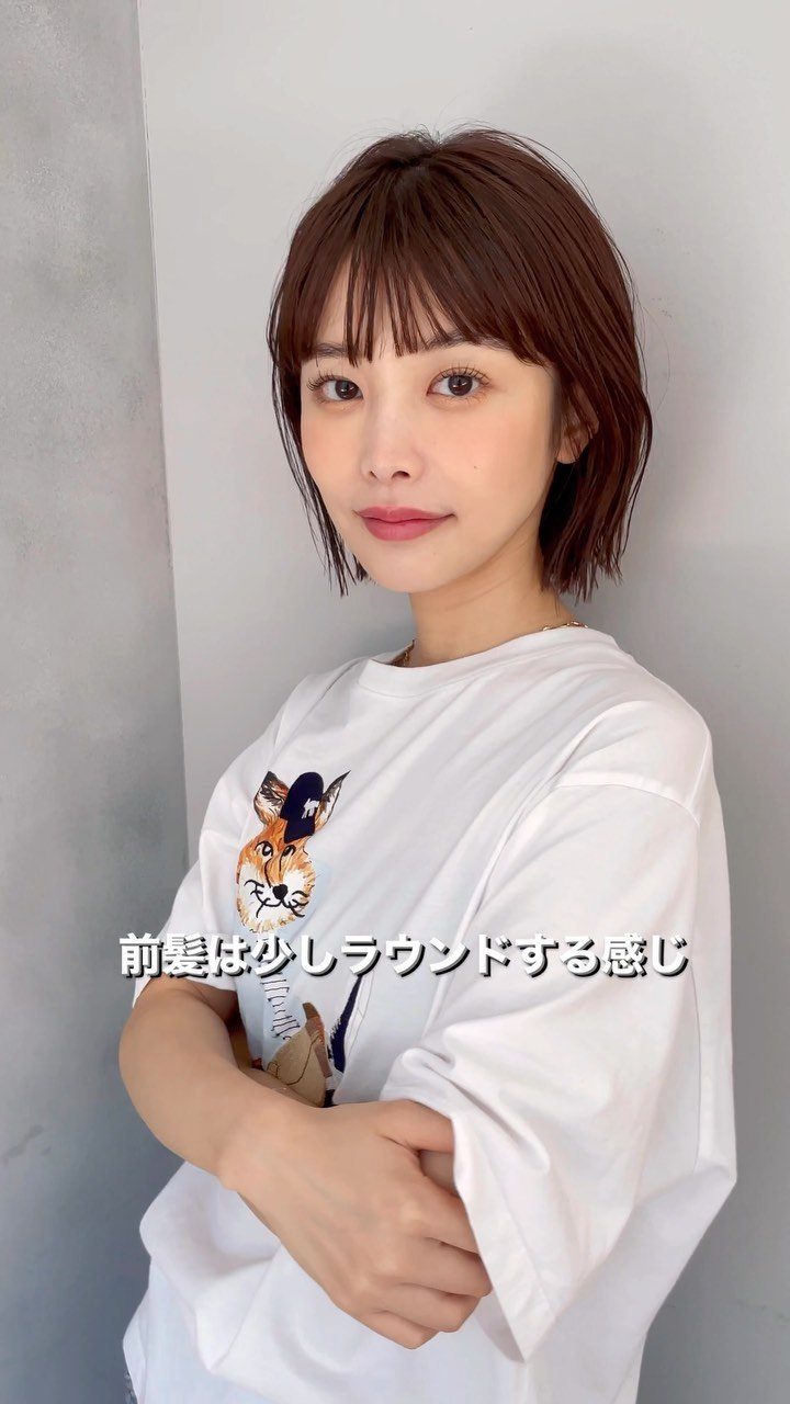 Woman with a short brown bob and wispy, rounded bangs against a gray wall