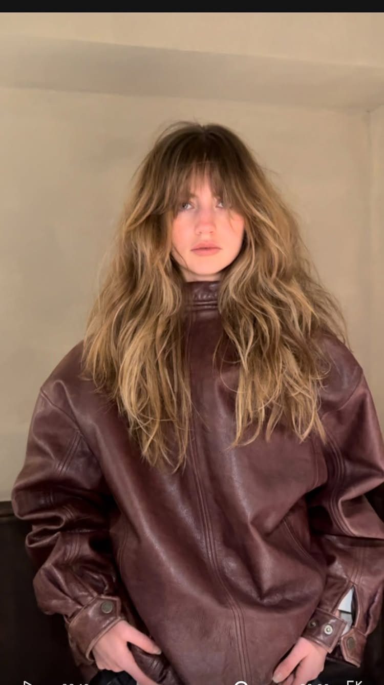 Long tousled layers frame uneven shaggy bangs and a dark leather jacket