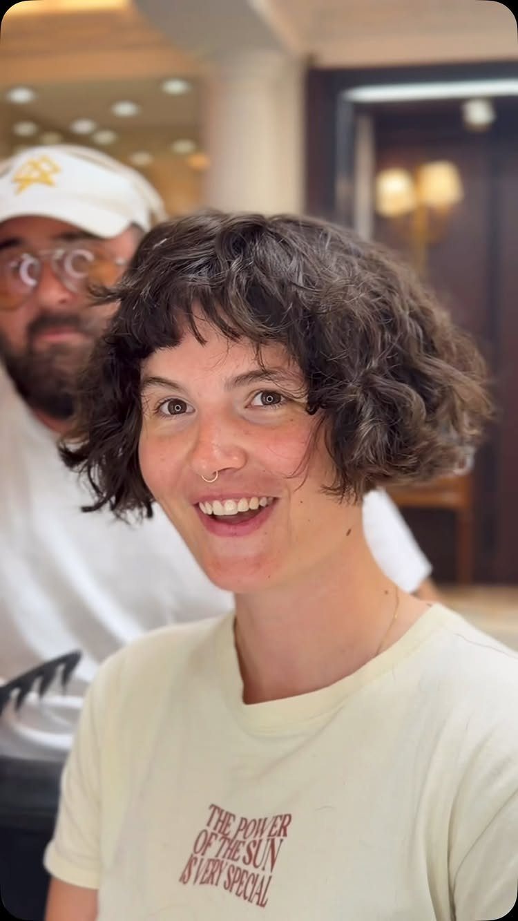 Smiling person showing a short curly jaw-length bob with tousled bangs in a salon