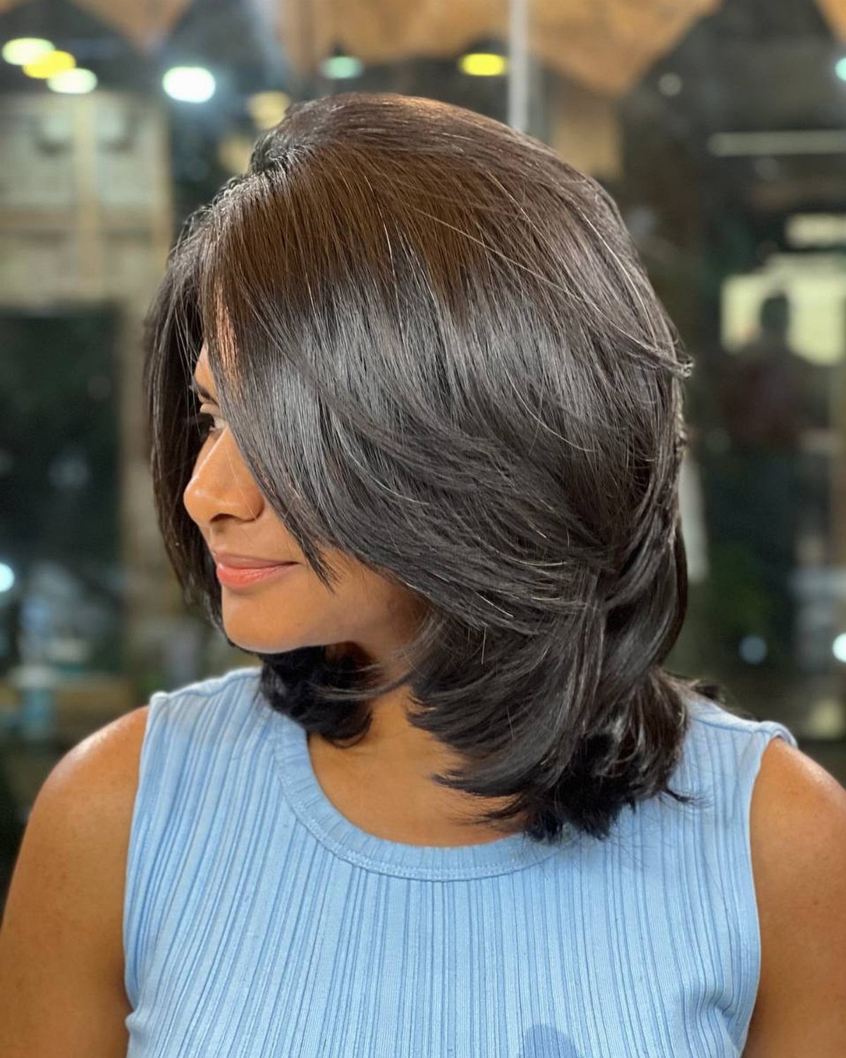 Woman showing a sleek, softly layered dark brown bob with side-swept bangs
