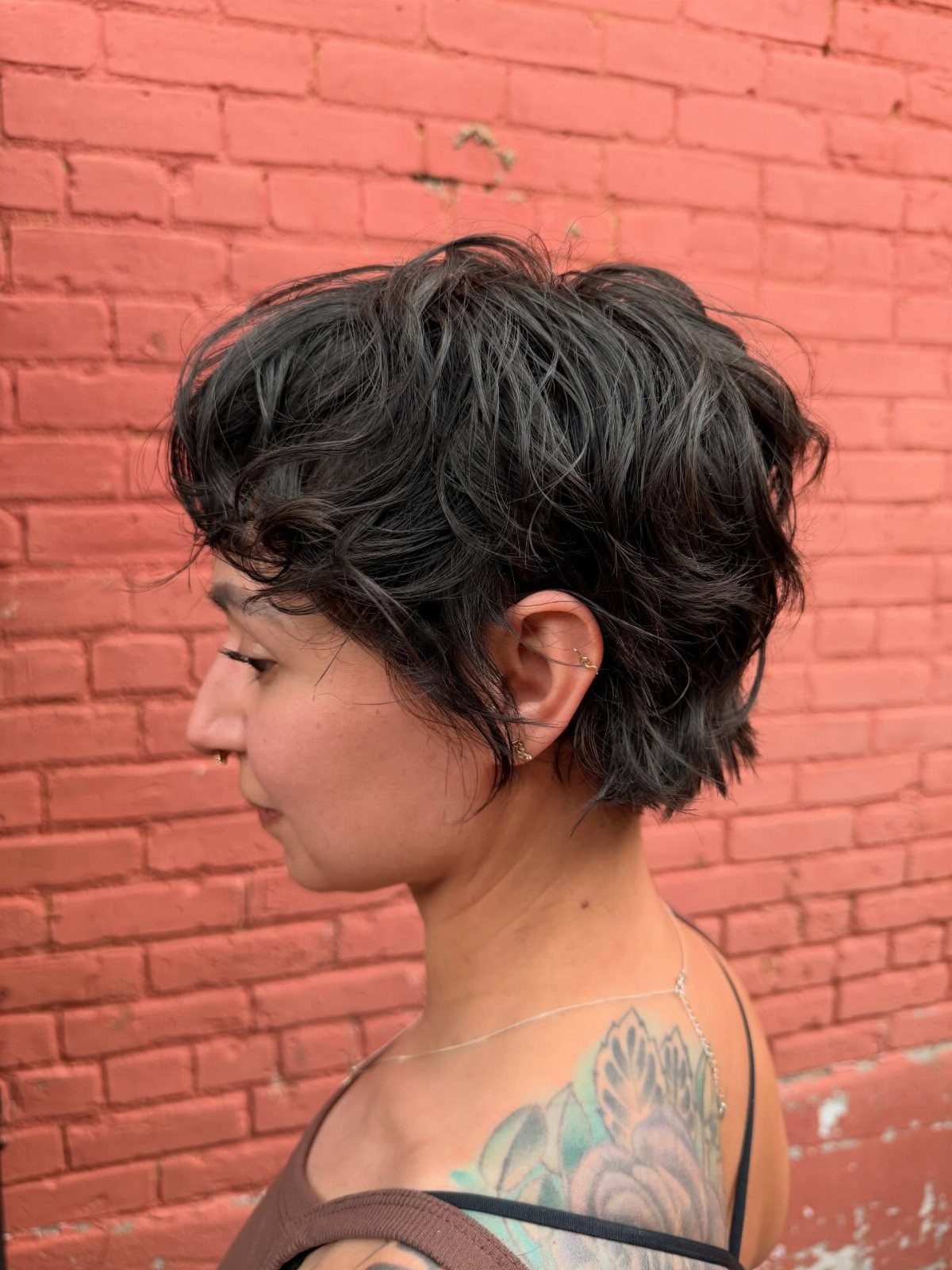 Short dark layered pixie-bob with textured fringe against a red brick wall
