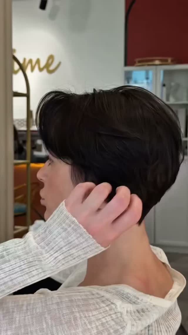 Short dark layered haircut shown in profile as a hand adjusts the hair