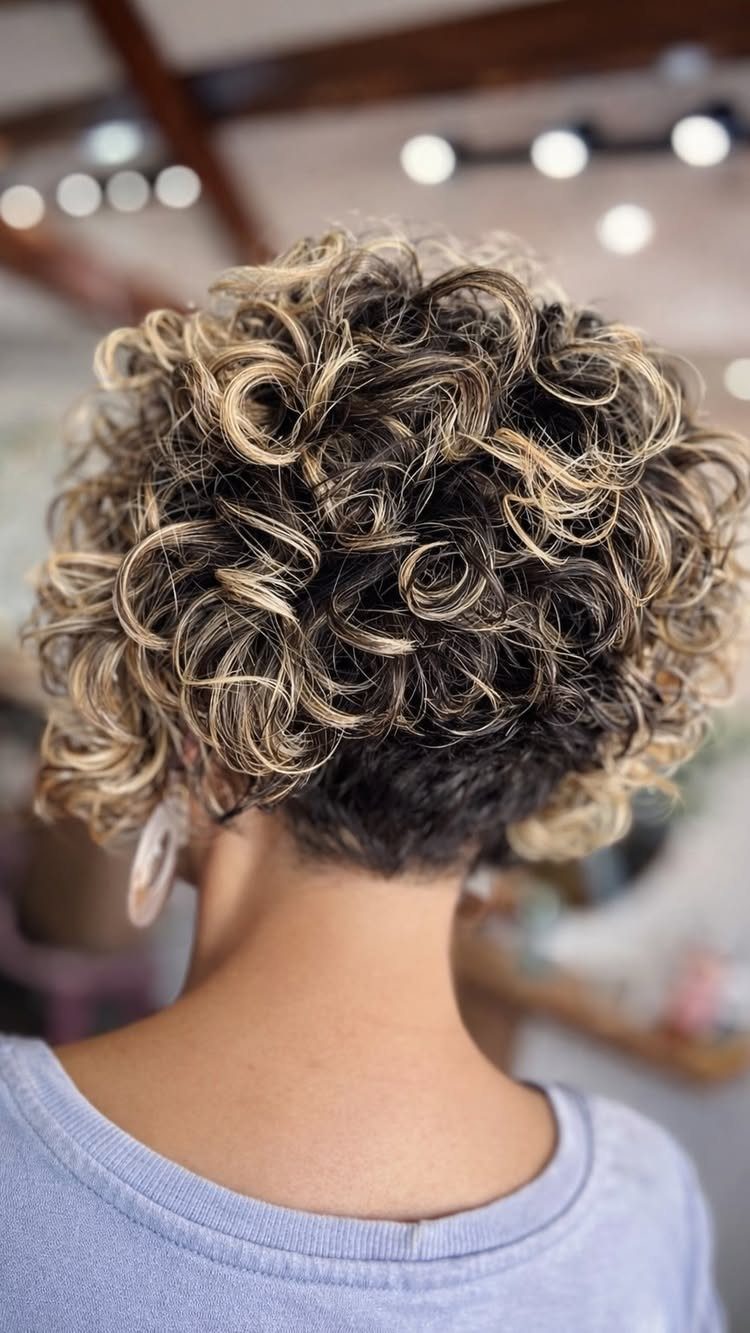 Short layered curls with blonde highlights viewed from behind in a salon