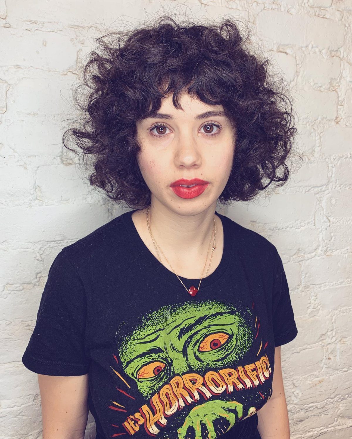 Woman with a short, rounded dark curly bob and full fringe