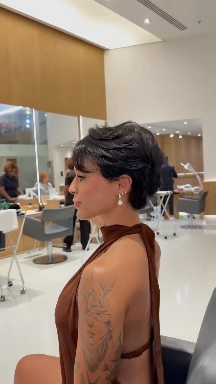 Woman with short dark layered hair seated in a bright salon chair