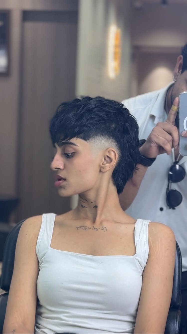 Woman with a textured dark pixie cut having her hair trimmed in a salon