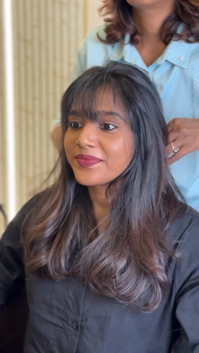 Woman with long layered dark hair and wispy bangs sitting in a salon chair