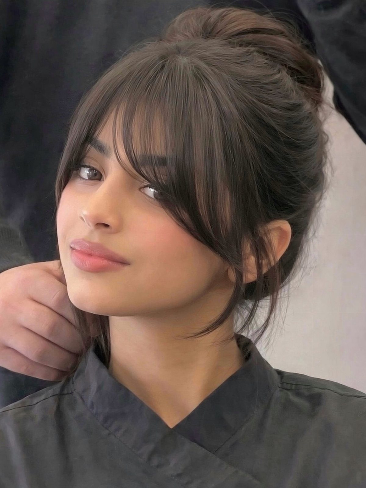 Young woman with wispy bangs framing her face and hair tied in a high bun