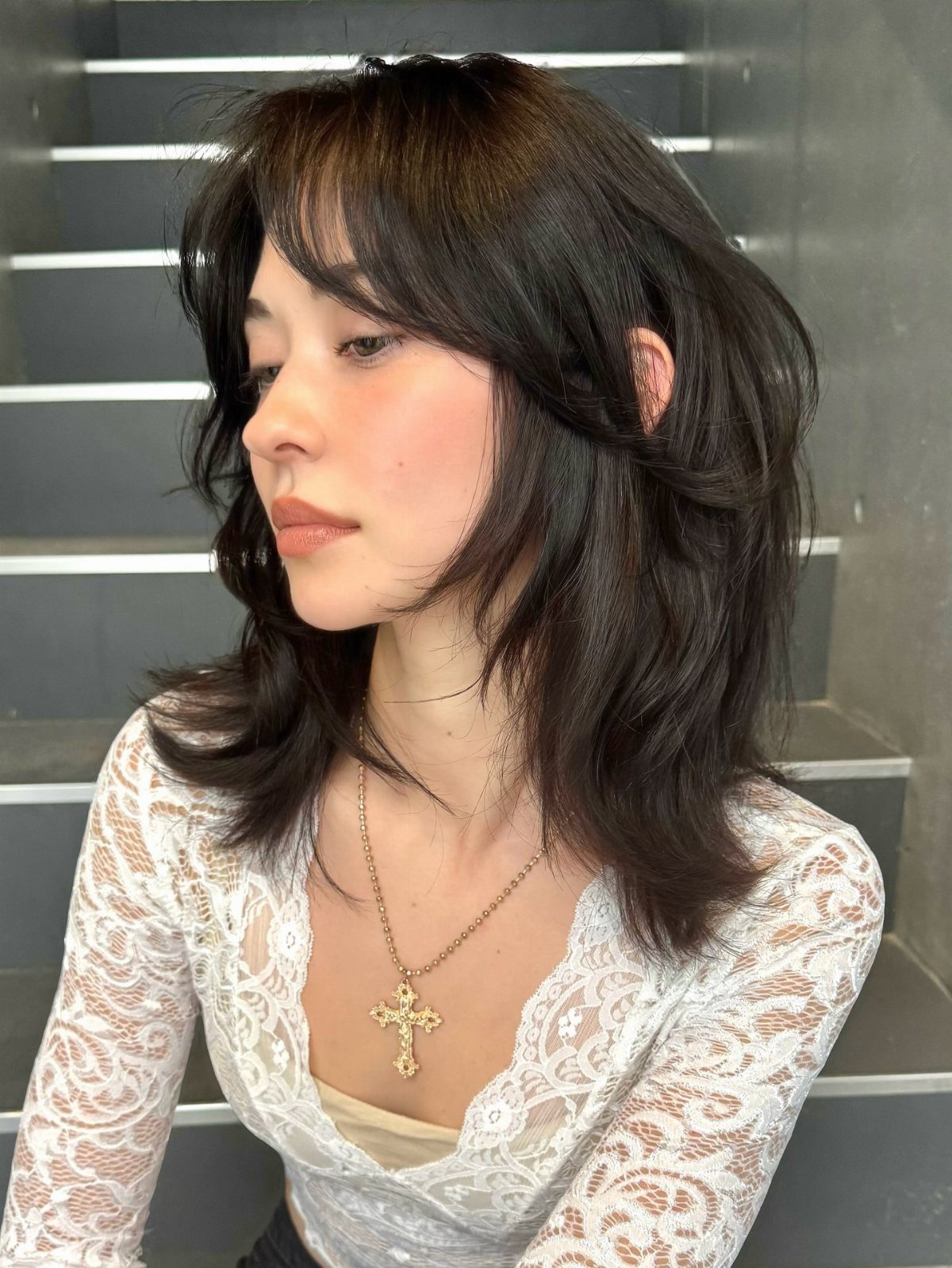 Woman showing a dark face-framing lob with curtain bangs and curled ends