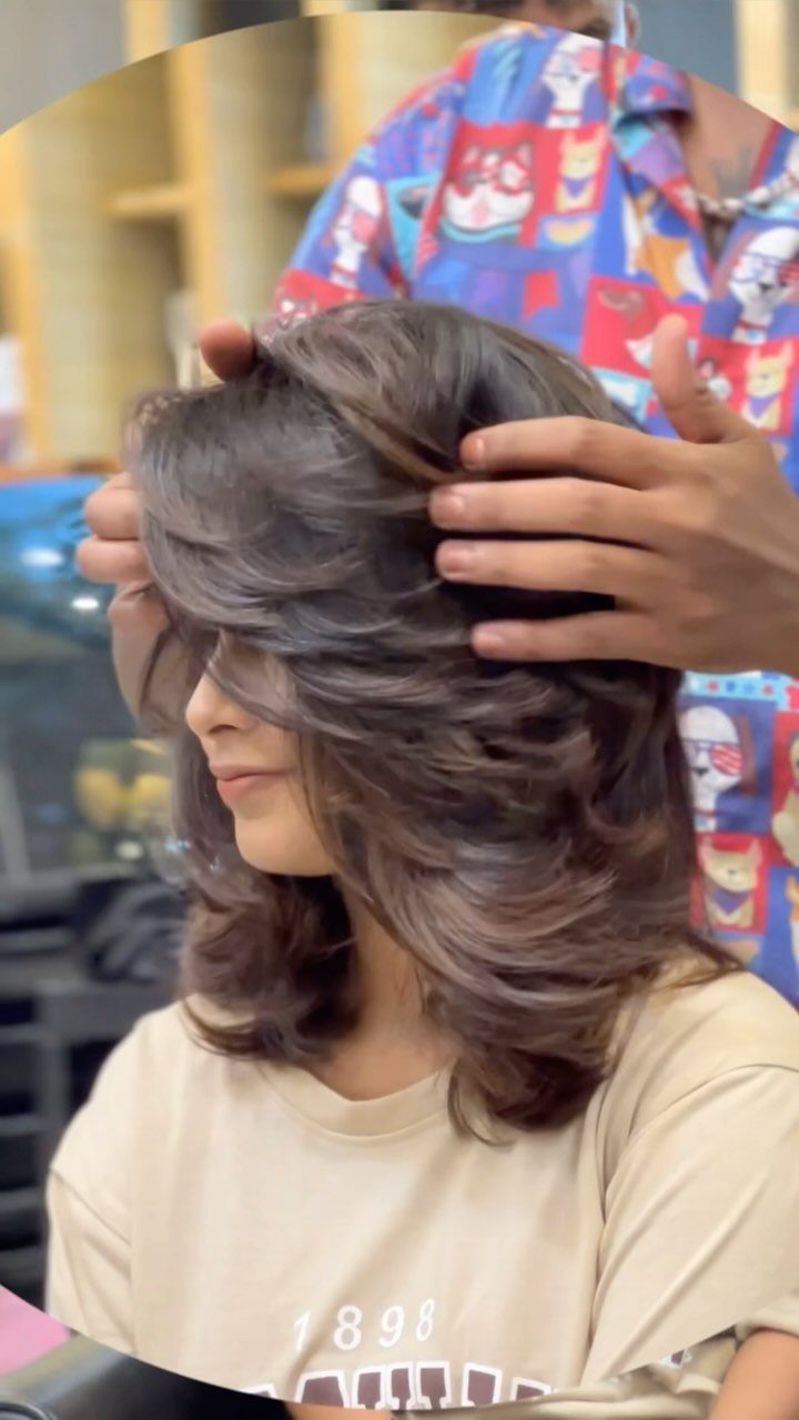 Woman with voluminous feathered brunette layers being arranged by a stylist in a salon