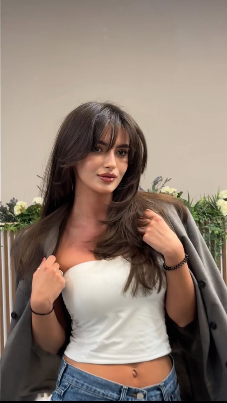 Woman showing long layered bangs and dark, face-framing hair