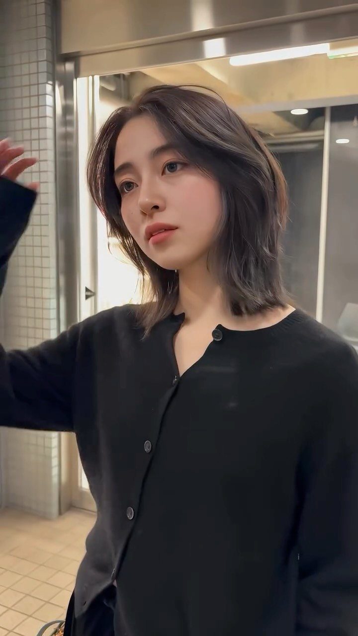Woman with a dark layered bob and face-framing pieces, wearing a black top