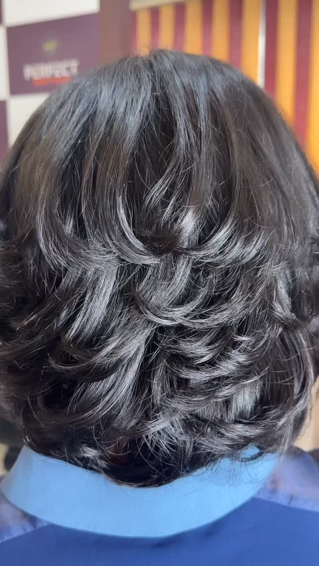 Dark shoulder-length hair styled in glossy, voluminous layers at a salon