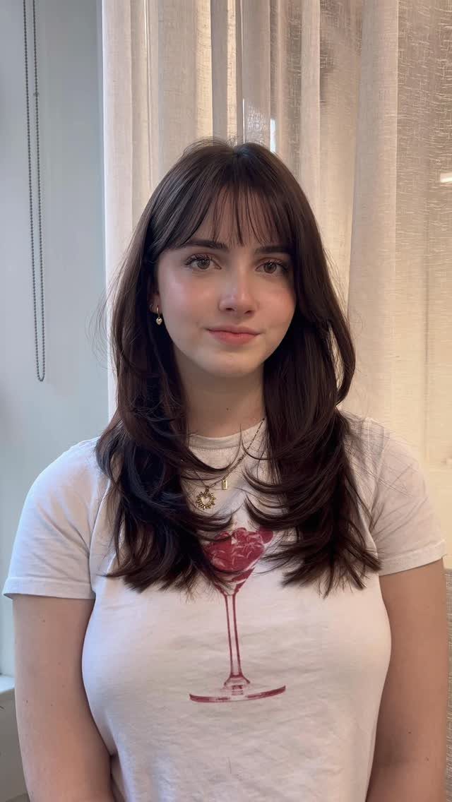 Woman displaying dark layered shoulder-length hairstyle with wispy bangs