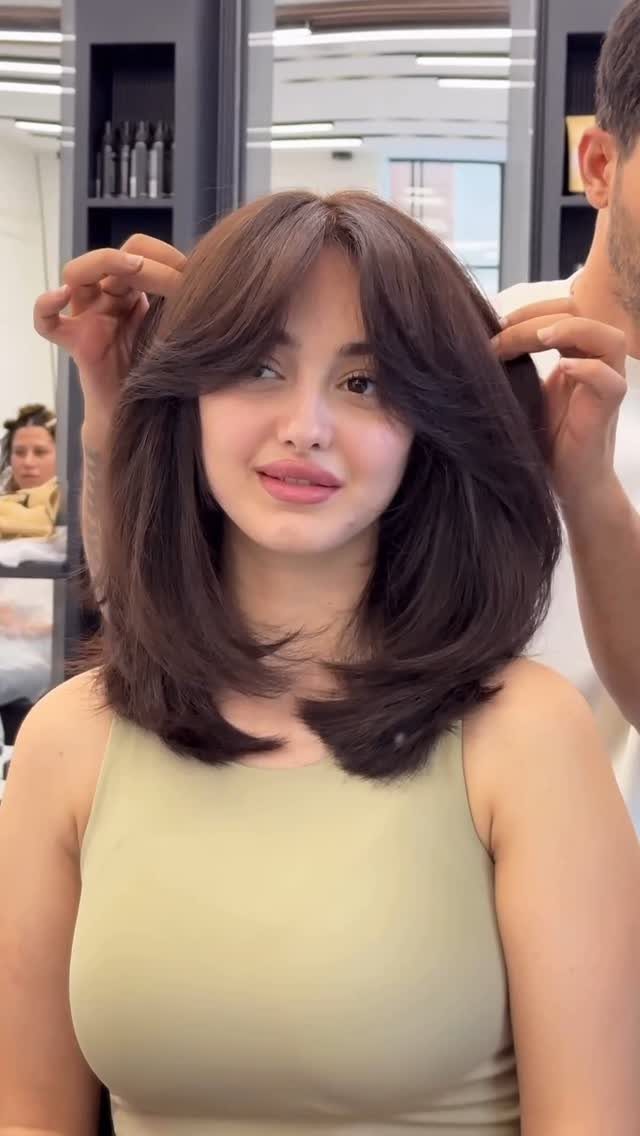 Woman showing voluminous layered brown hair with a parted, swoopy fringe