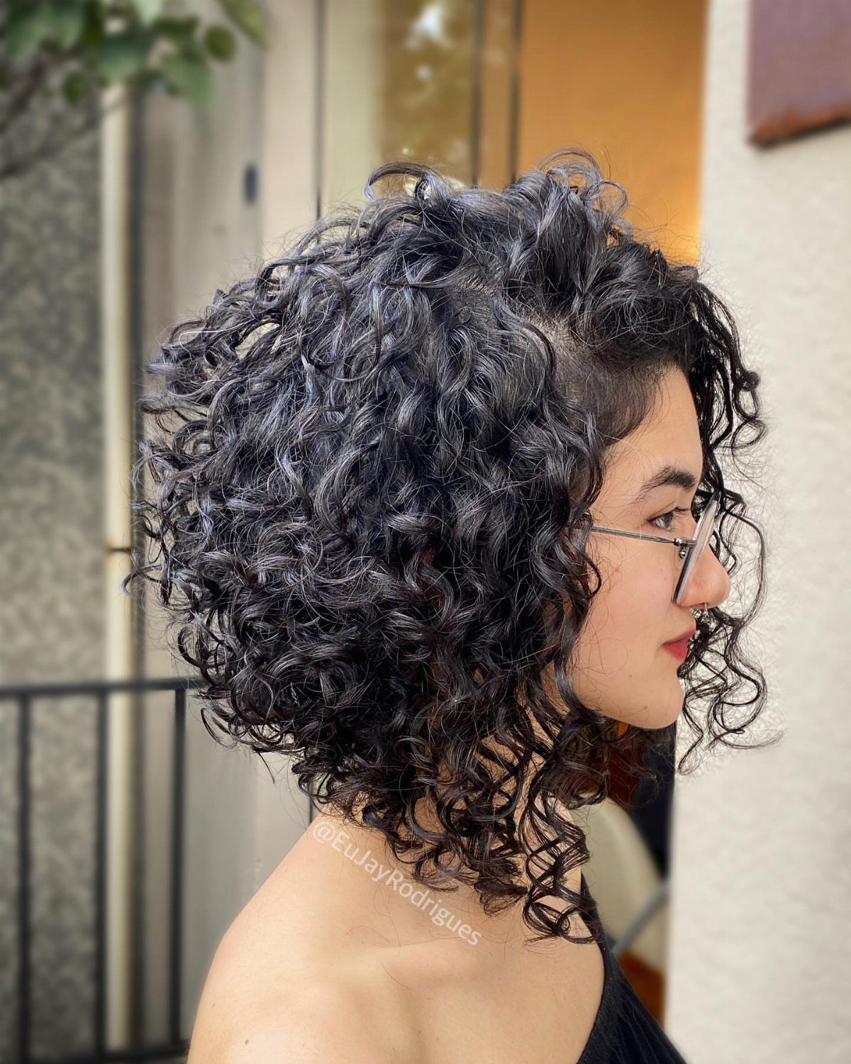 Side-profile person wearing glasses with a rounded, curly layered bob haircut