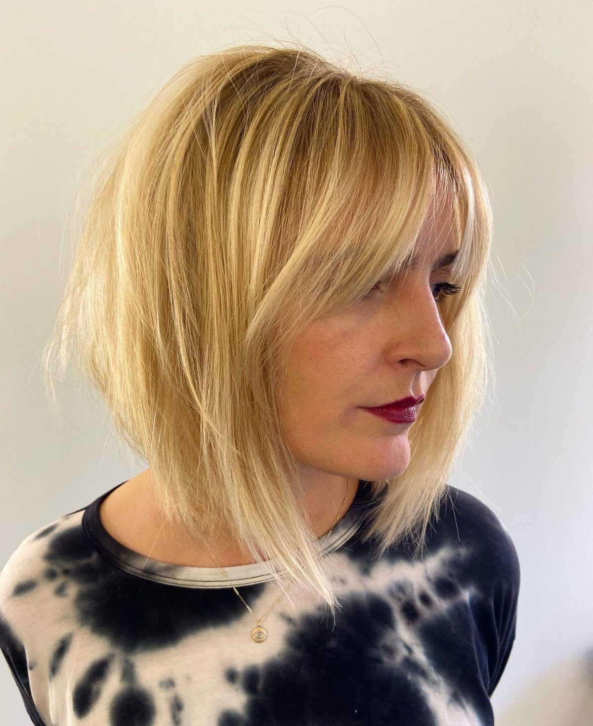 Woman showing blonde layered bob with wispy bangs and textured shoulder-length ends
