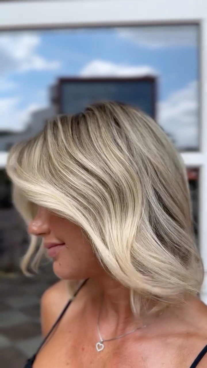 Woman showing a layered blonde bob with darker roots and sweeping side bangs