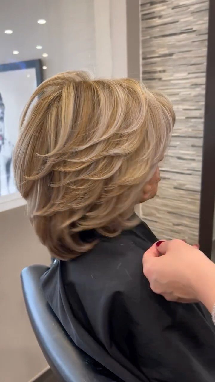 Short blonde balayage bob with distinct layers, shown from behind in a salon.