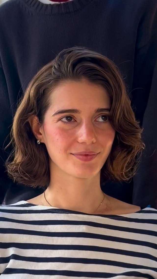 Woman with short wavy layered brown bob and side part wearing a striped top
