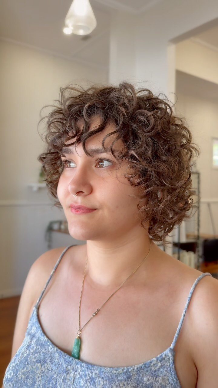 Short curly bob with wispy bangs framing a person's face