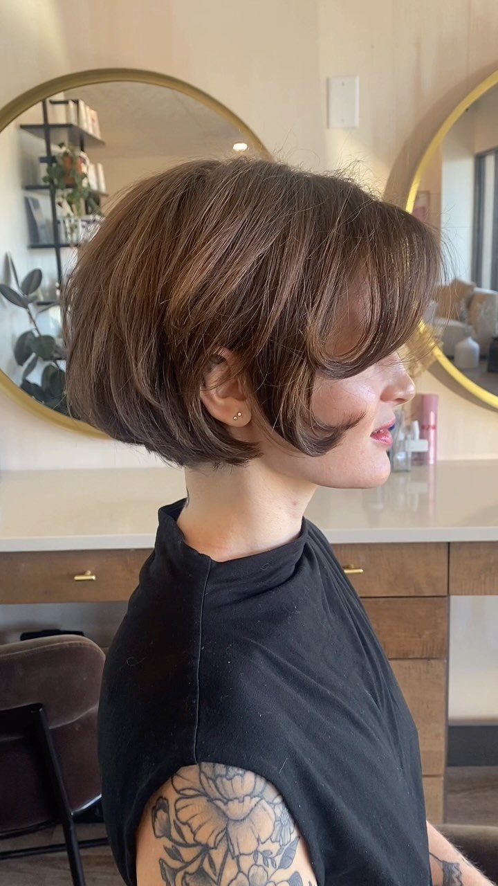 Woman showing a softly layered, jaw-length brown bob with long fringe