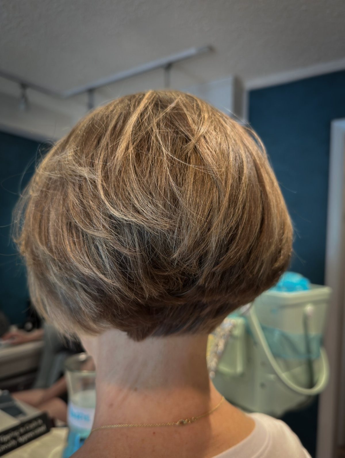 Short layered brown bob shows feathered texture and a rounded nape in a salon