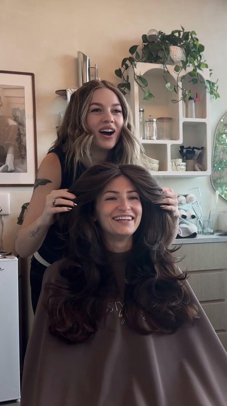 Hairstylist arranges long, voluminous brunette layers with curled ends in a salon