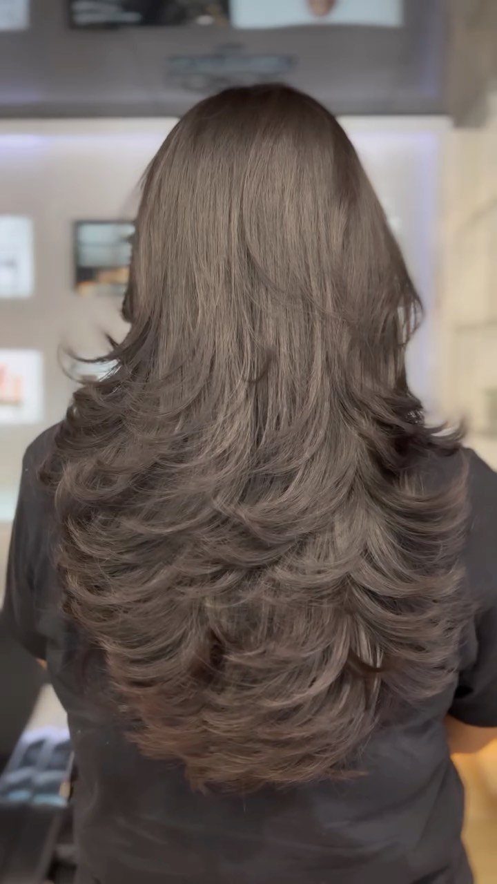 Long brown hair falls in glossy, cascading layers with curled, flipped ends.