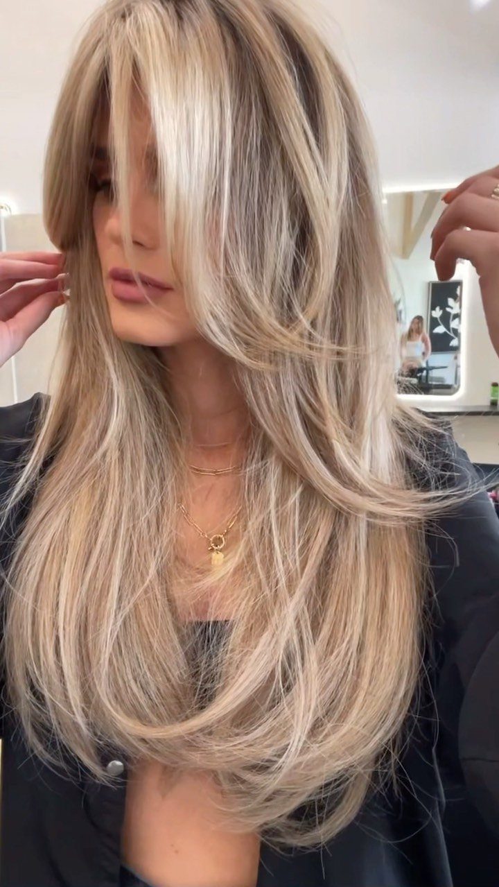 Woman displaying long blonde face-framing layers with feathered, sweeping ends