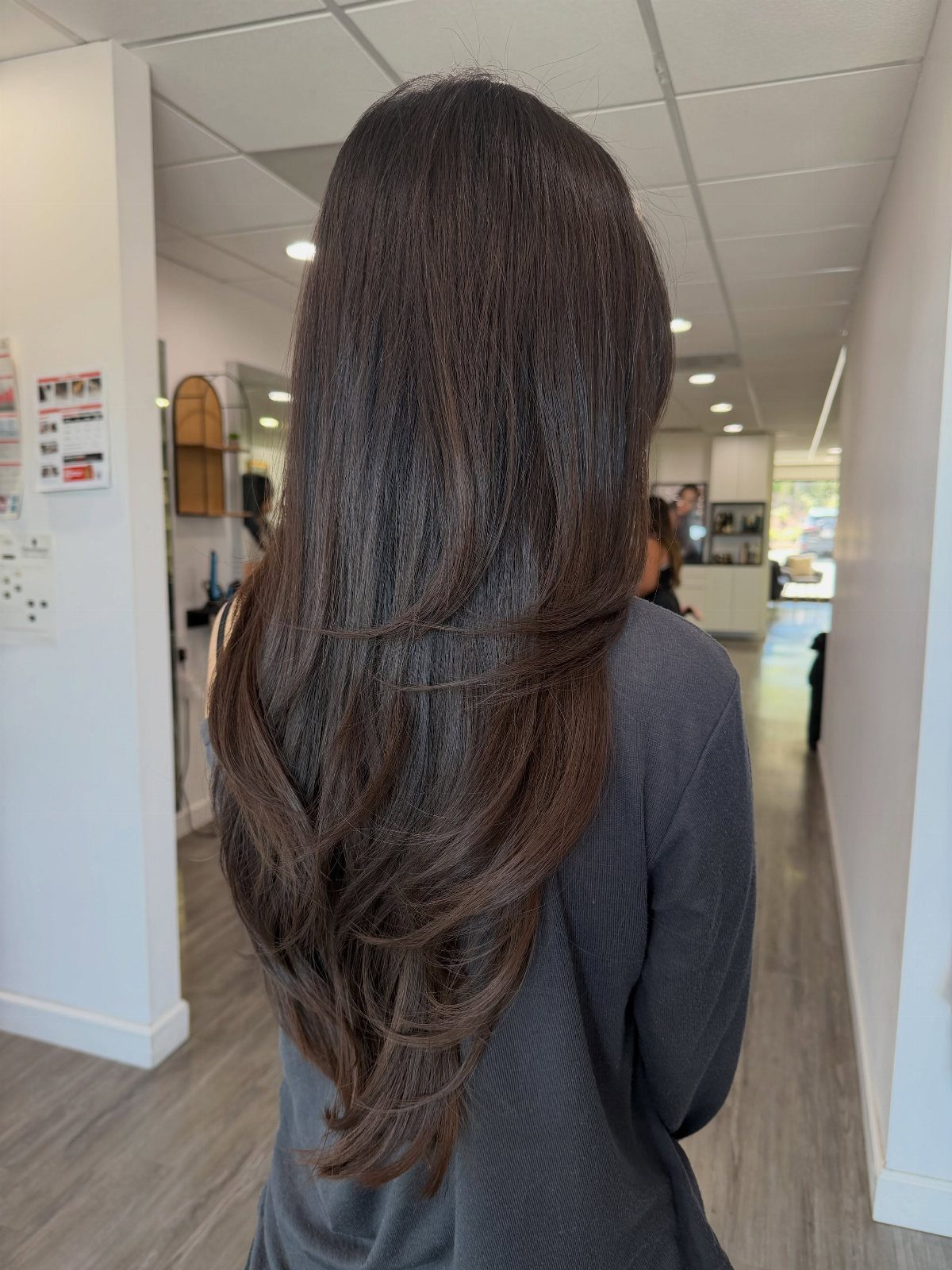 Long dark brown hair falls in curved, graduated layers down the back in a salon