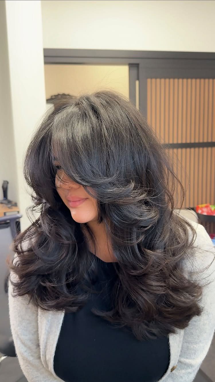 Woman with long dark hippie layers, sweeping bangs, and voluminous curled ends