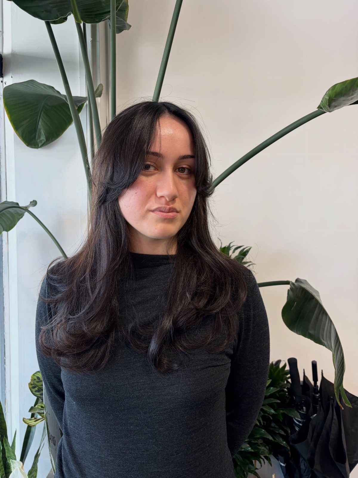 Long dark hair with softly layered ends frames a person in a black top.