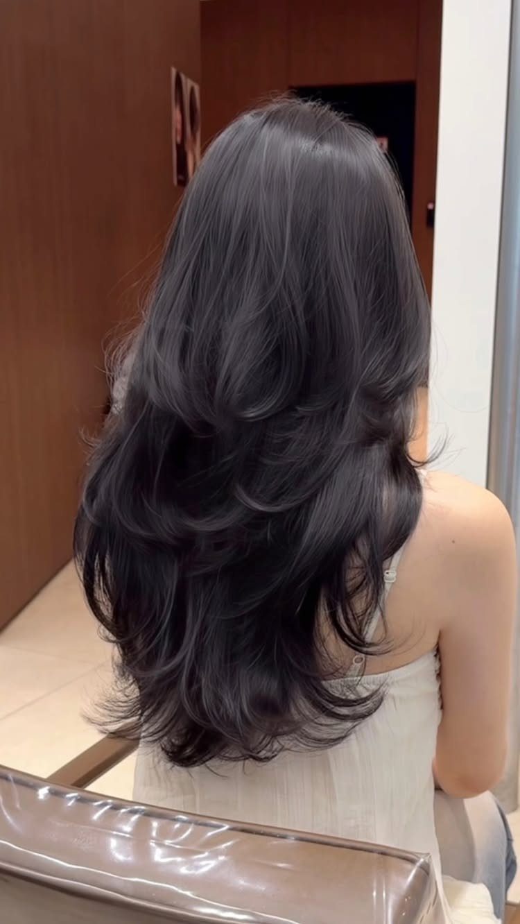 Long dark hair falls in separated, curled layers over a white sleeveless top.