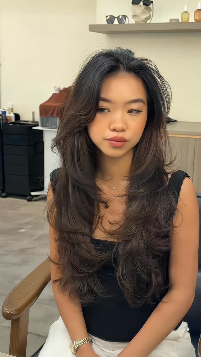 Woman seated in a salon with long, dark hair in soft blended layers