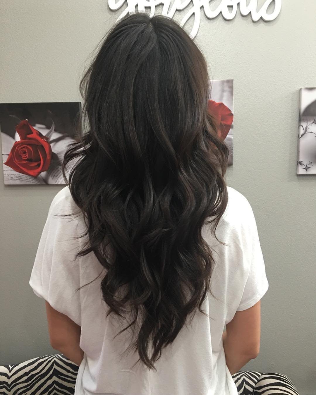 Long dark wavy hair falls in cascading layers to a pointed V-shaped back perimeter