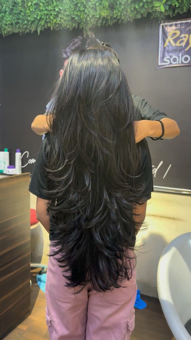 Long dark hair with soft cascading layers and curled ends, shown from behind in a salon.