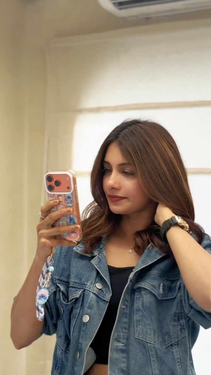 Woman with medium-length chestnut waves taking a mirror selfie